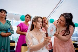 Wedding party gathered under a white tent with teal balloons and decorations for a celebration.