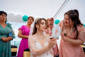 Celebration scene with wedding guests in colorful dresses under a white tent with teal decorations.