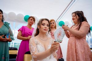 Festive wedding reception scene with guests in pastel dresses under white tent with teal balloons.
