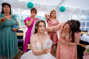 Wedding reception scene with guests in colorful dresses under white tent with teal accents.