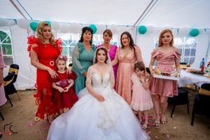 Wedding party in colorful dresses gathers under a white tent decorated with teal balloons.