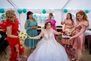 Wedding celebration with bridal party in vibrant dresses under tent with teal balloon decor.