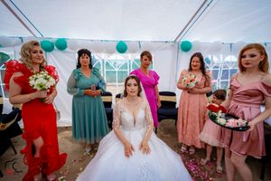 Bridal party in coordinated pink and red dresses gathered around bride in white gown.