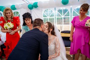 Tender moment during wedding ceremony under tent with teal and white balloon decorations.