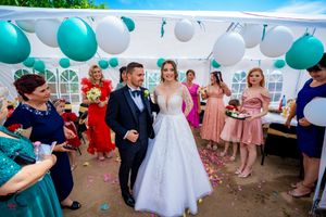Wedding party celebrates under outdoor tent decorated with teal and white balloons.