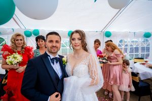 Wedding party gathered under teal and white balloon decorations in a bright reception tent.