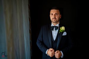 Groom adjusting his bowtie in dramatic low-key lighting.