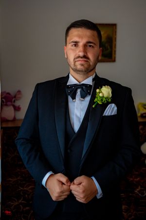 Groom in three-piece tuxedo with boutonniere preparing for wedding day.