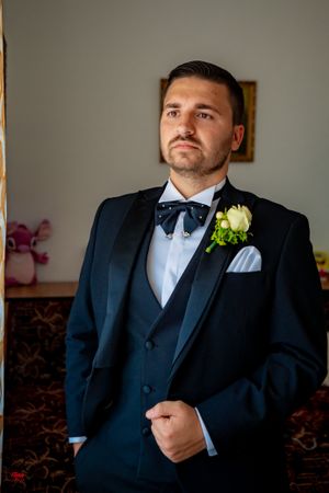 A groom in a classic black tuxedo and bow tie poses during wedding preparations.