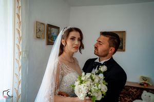 A wedding couple shares an intimate moment with a white bouquet against a light background.