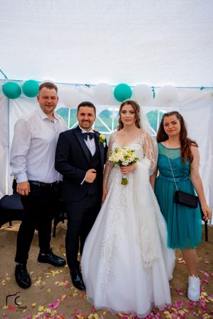 Wedding guests and party members pose together under a tent decorated with teal balloons.