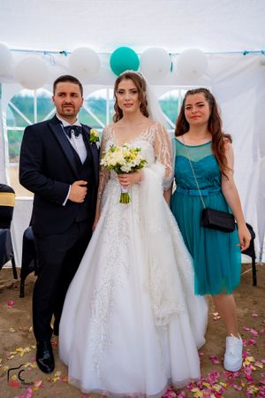Wedding celebration under a white tent with teal accents and scattered rose petals on the ground.