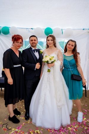 Wedding party members gather for photos under a decorated tent with teal balloons and pink petals.