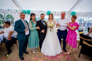 Wedding celebration in a white tent with turquoise balloons and guests gathered around a bride in a white gown.