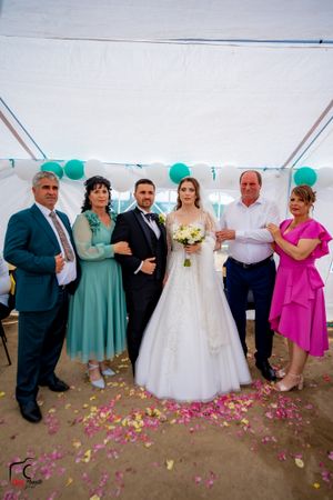 Wedding party posing together under a white tent with scattered pink and yellow flower petals on the ground.
