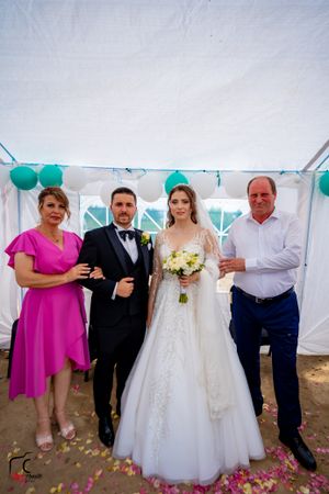 Wedding group photo in a tent decorated with teal balloons and rose petals scattered on the floor.