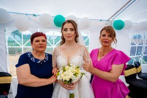 Wedding party members in formal attire standing together under a white tent with green balloon decorations.