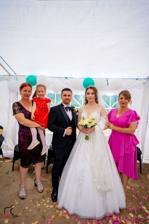Wedding party members posing in a white tent with turquoise balloons and rose petals on the floor.