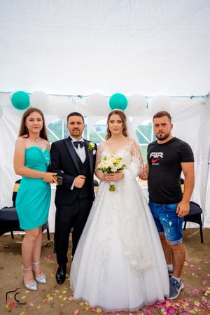 Wedding party members posing together in casual and formal attire under a decorated white tent.