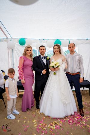 Wedding group photo with guests in formal wear and a white tent decorated with turquoise balloons.