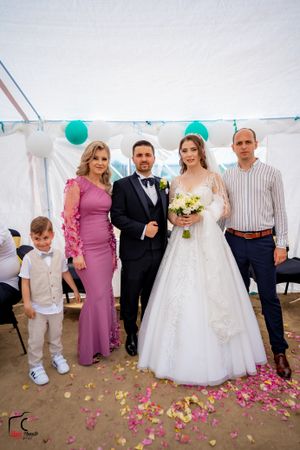 Wedding party poses together in a tent with pink flower petals scattered on the ground and teal balloons as decor.