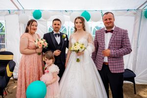 Formal wedding gathering under white tent with teal balloon decorations and pink scattered petals.
