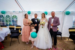 Wedding party poses in tent with teal balloons and white decor for formal photographs.