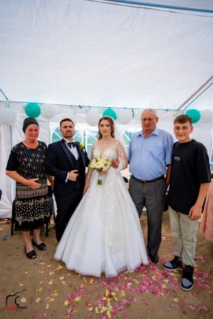 Wedding guests gather for group photos under white tent with scattered pink petals on ground.