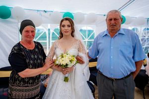 Wedding party members pose together under white tent with teal balloon decorations.