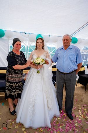 Wedding photo session showing bride in white dress posing with guests under a white tent with teal decorations.