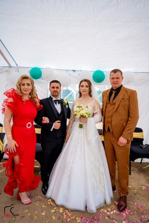 Wedding guests in formal attire pose with bride in elegant white gown under tent with teal balloons.
