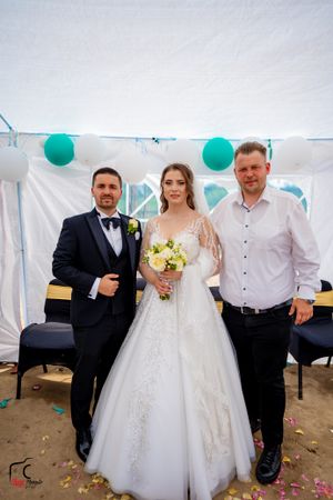 Wedding party members pose with bride in traditional white dress under decorated tent with scattered petals.