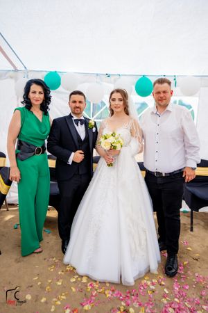 Wedding celebration with guests in formal attire posing alongside bride under white tent with teal accents.