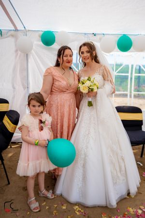 Wedding party members in pink dresses pose with bride under tent with teal balloon decorations.