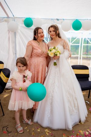 Wedding celebration showing bride and guests in pink attire posing under decorated white tent.