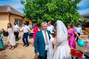 Festive wedding celebration with dancing guests in colorful outfits under a green tree.