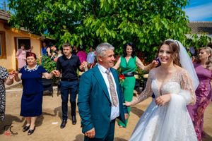 Joyful outdoor wedding celebration with guests dancing under a lush green tree.