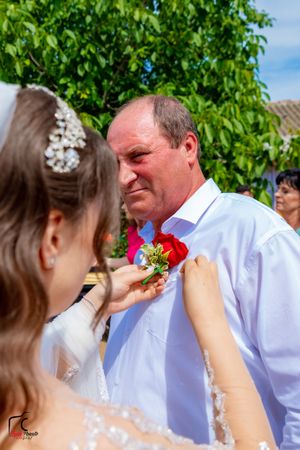 Wedding guest receiving boutonniere pinning during outdoor celebration.