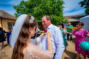 Boutonniere pinning moment during outdoor wedding celebration under green tree.