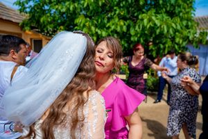 Joyful wedding celebration scene with guests in colorful attire under leafy green trees.