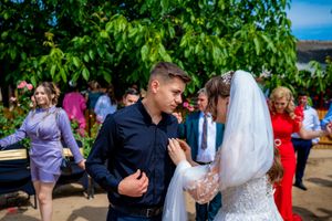 Wedding guests mingle and celebrate during an outdoor reception by a yellow building.