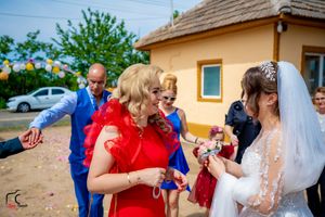 Wedding celebration with guests in vibrant red and blue outfits throwing confetti outdoors.