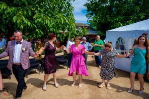 Celebratory group dance at outdoor wedding with lush green trees in background.