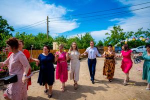 Wedding guests form dancing line at outdoor venue with white tent and blue sky backdrop.