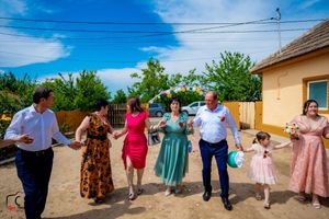 Wedding guests dancing in a traditional line dance outdoors near a yellow building.