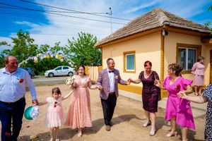 Festive group dancing together in a line outside a yellow house during a celebration on a sunny day.