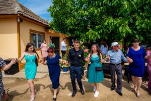 Joyful dancers holding hands in a line during an outdoor celebration near a yellow building.