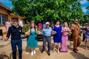 Festive group dance line forming outside under green trees at a celebration event.