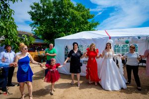 Wedding celebration with guests dancing in a line near a white tent outdoors.