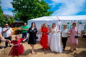 Wedding party and guests performing a dance line near a white tent during outdoor reception.